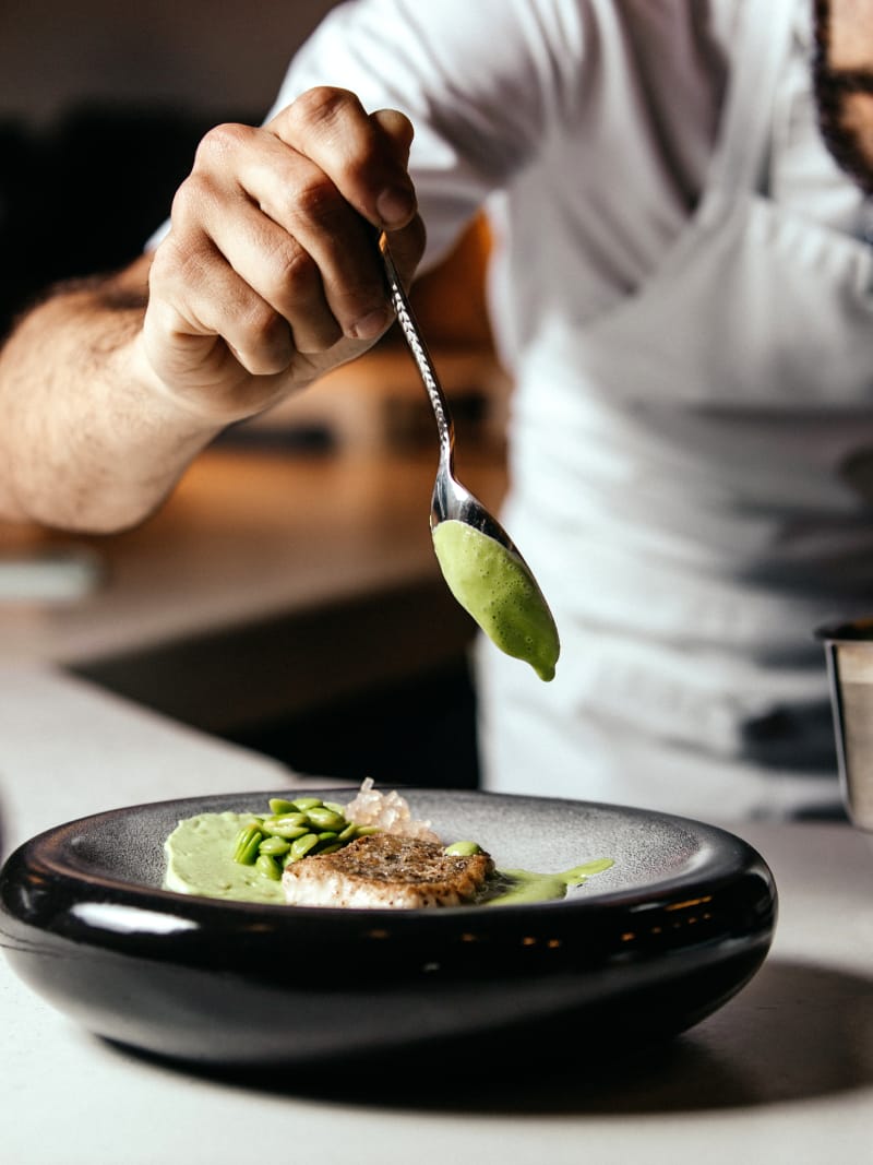 Chef che guarnisce un piatto di pesce con crema verde nella cucina del ristorante Le Contrade
