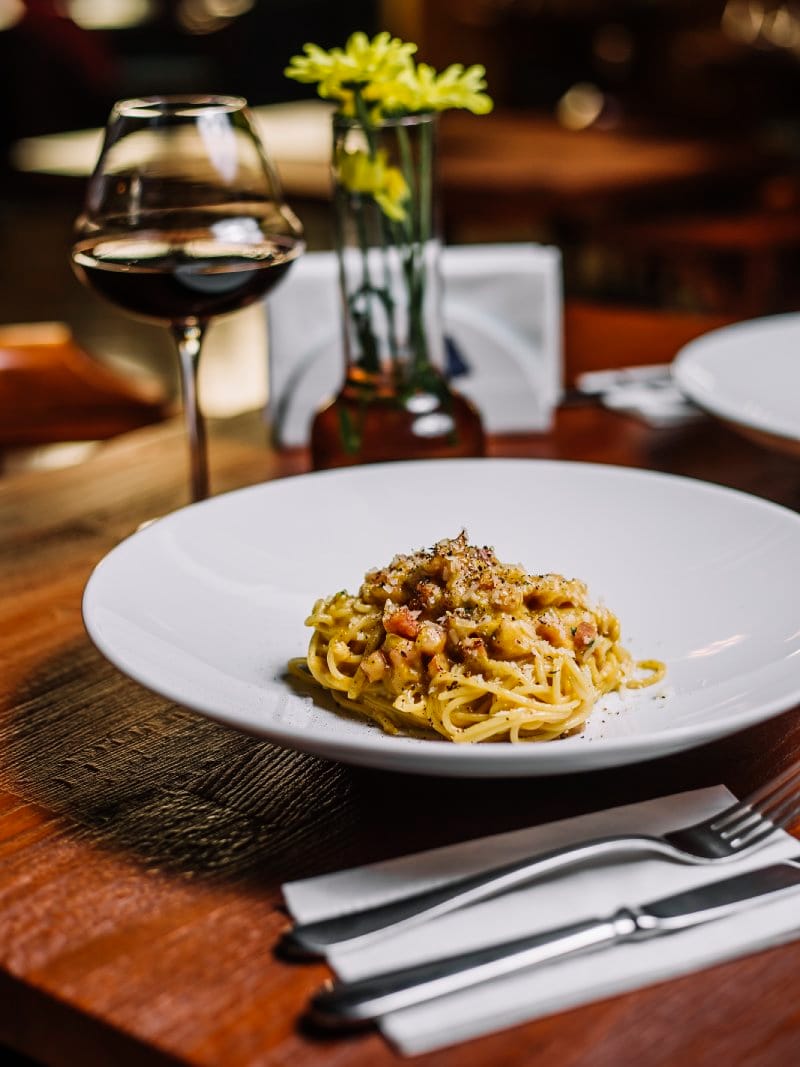 Spaghetti alla carbonara serviti al tavolo del ristorante Le Contrade con calice di vino rosso